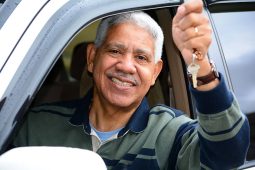 Person smiling in the driver's seat of a car with the window down, holding the keys up