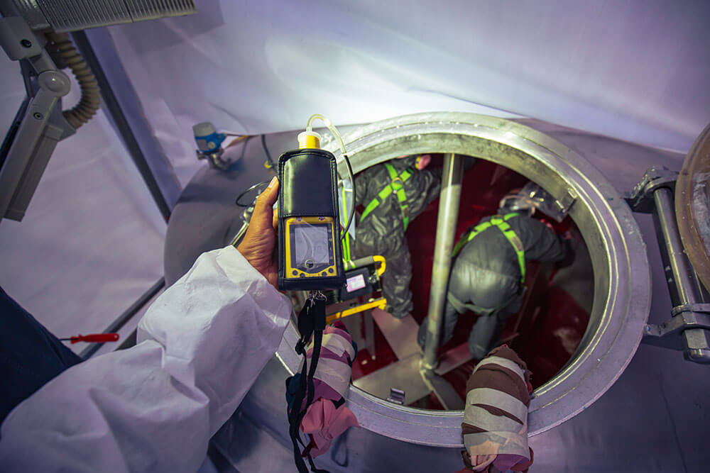 Worker hand holding gas detector inspection safety gas testing at front manhole stainless tank