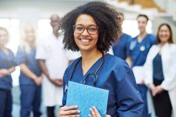 Healthcare worker standing in office hallway with other healthcare workers standing behind